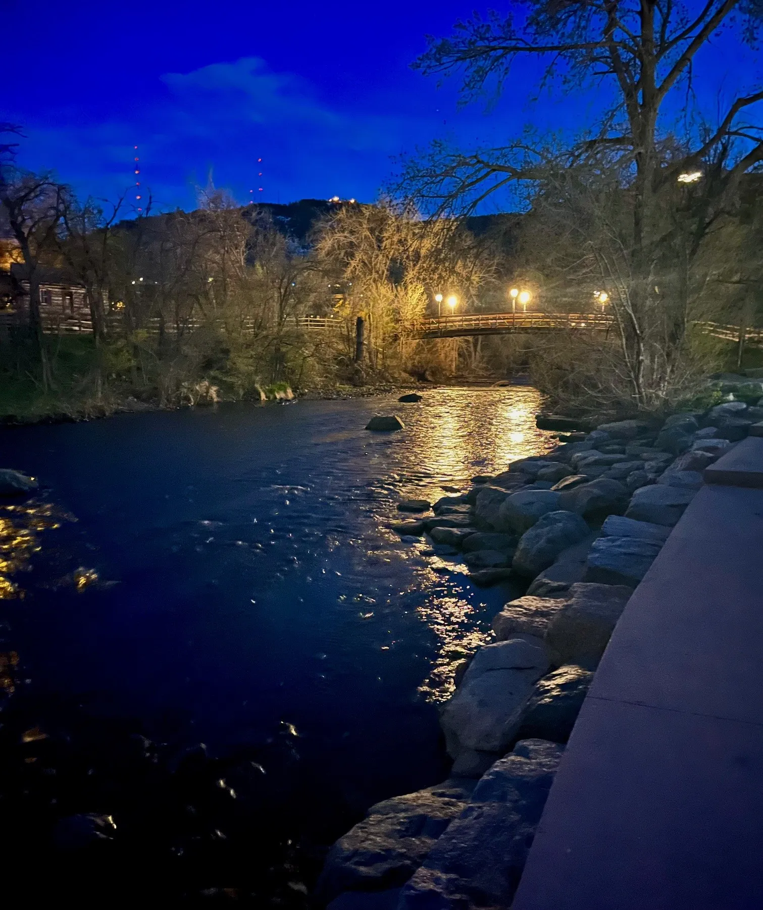 nearly-dark view of Clear Creek with lights from the pedestrian bridge reflected on the water