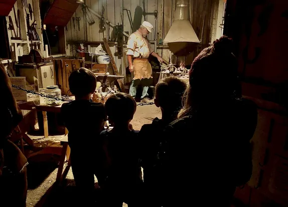 children gathered in the doorway, watching the blacksmith at his forge - tools hanging from the walls