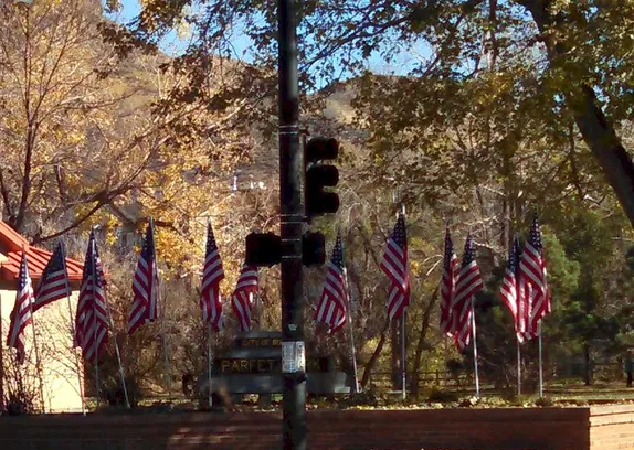 A dozen American flags on poles in the corner planter at Parfet Park.  Fall folliage and South Table Mountain in background.