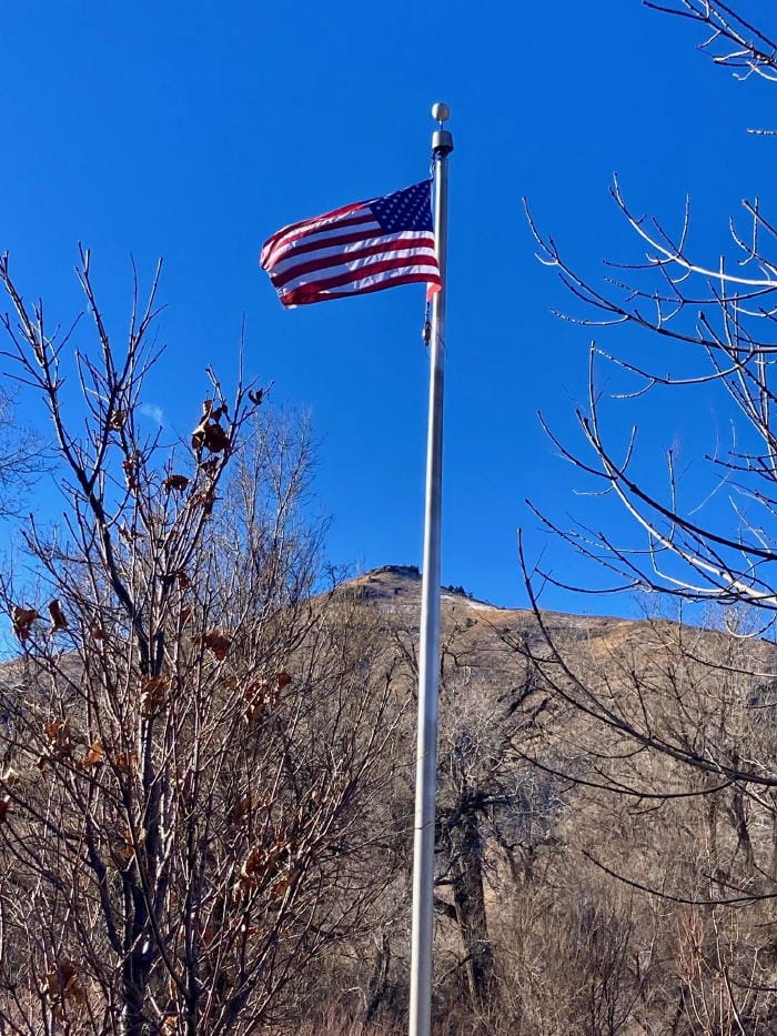 American flag against a bright blue sky with leafless trees and Mt. Zion in the background.