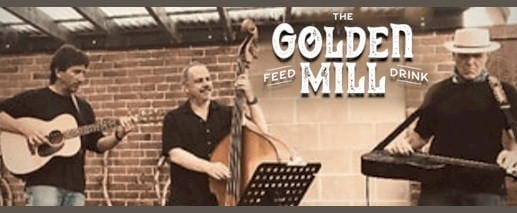 3 men with stringed instruments standing in front of a brick wall - The Golden Mill logo