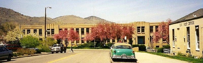 1930's-era 2 story school with pink flowering trees in front.  U.S. Post Office appears on right side, along with aqua car from 1950s.
