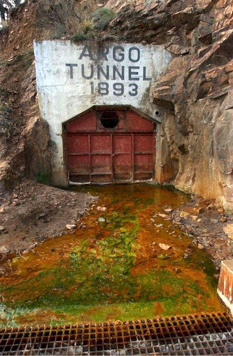 Argo Tunnel 1894 - concrete portal with metal door, water coming out from the bottom, going into a storm grate
