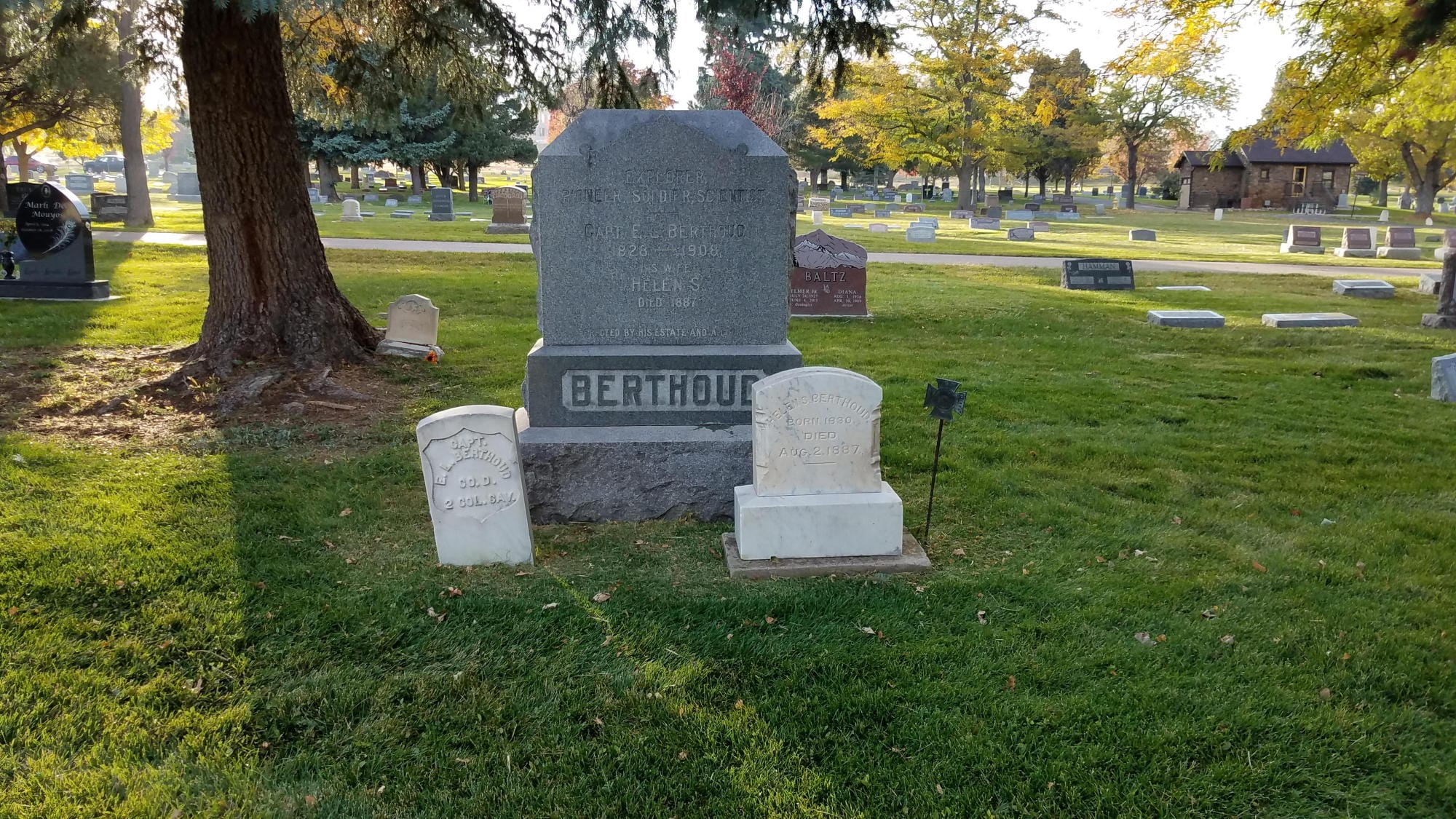 Large gray headstone saying "BERTHOUD" with two smaller white stones in front.  Cemetery in the background with leaves starting to change.