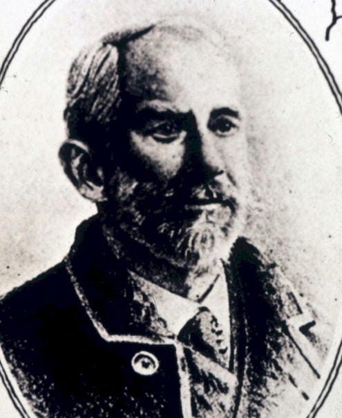 grainy black and white photographic portrait of a man with a beard, wearing a coat and tie
