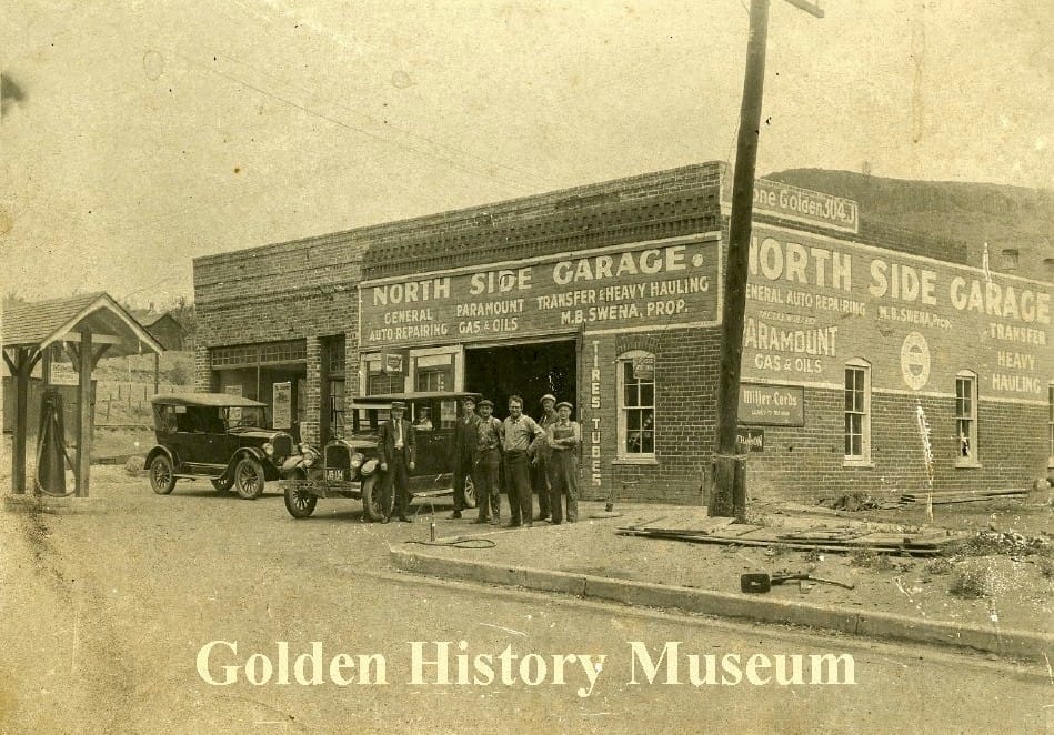 Four men stand in from of a brick building marked North Side Garage.  1920s-era cars and one gas pump in front of the building.