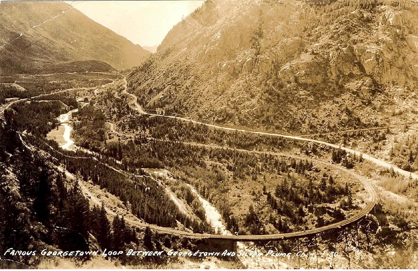 Sepia-toned postcard showing tracks looping through pine forest and over a creek.