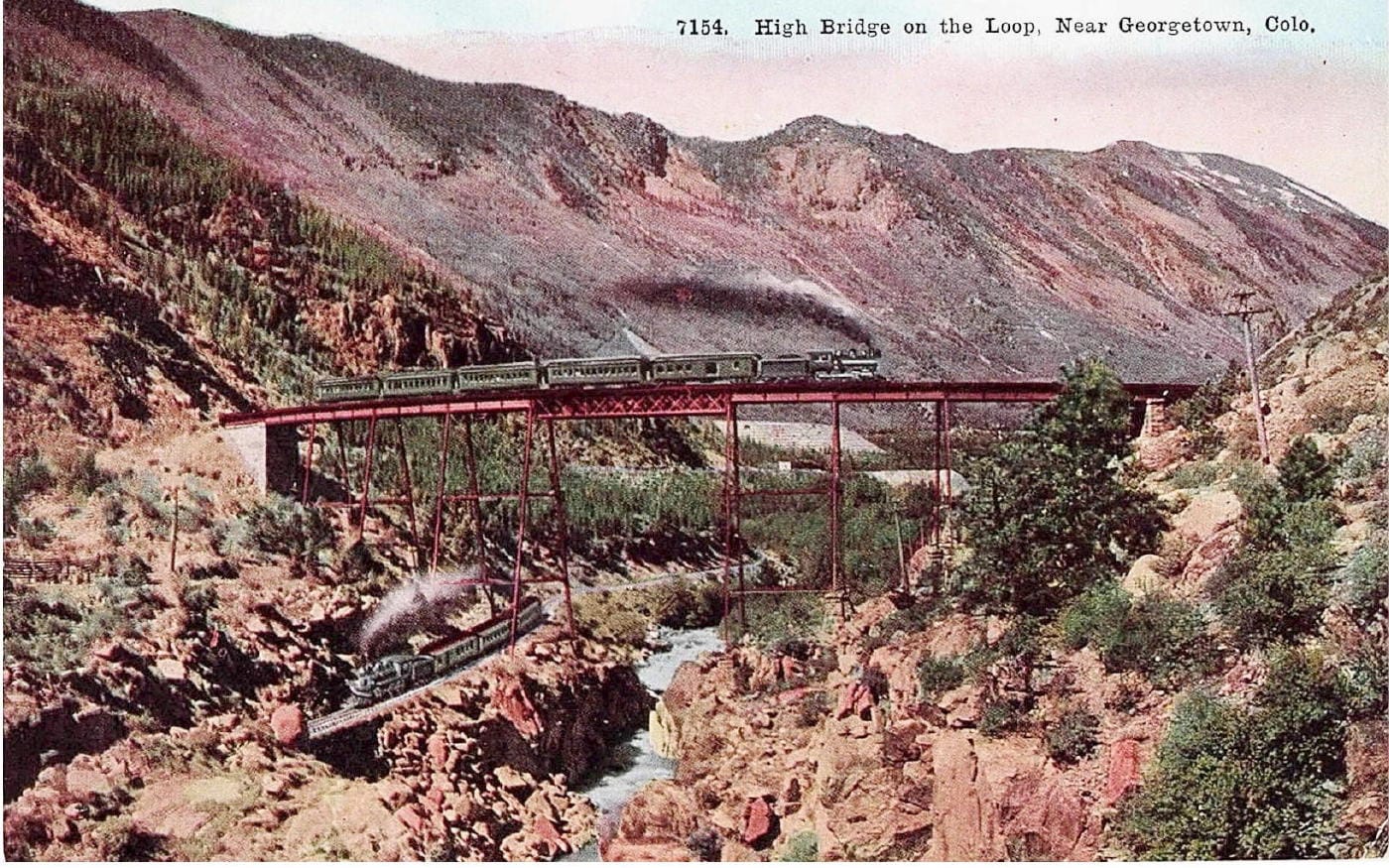 Hand-tinted postcard shows the Loop bridge with one train passing over and another passing under.