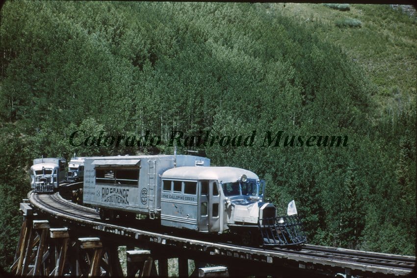 3 "Galloping Geese" on a high railroad trestle, forested mountainside in the background