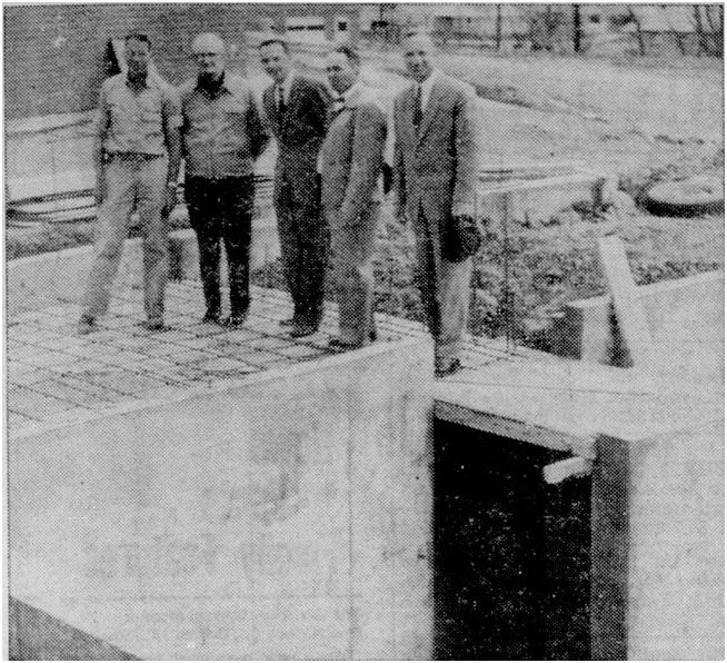 Five men stand on a construction site on a slab of concrete over an underground chamber.