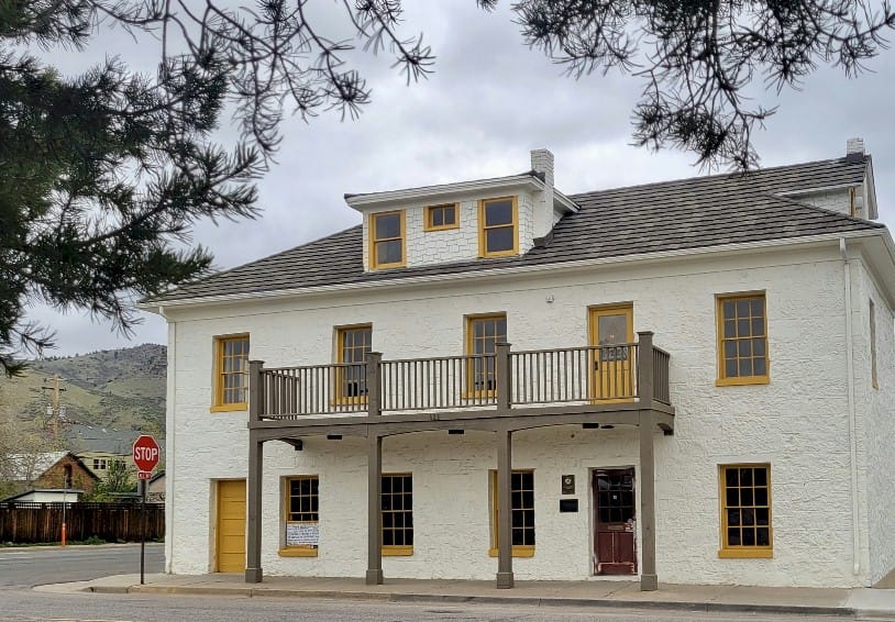 Two story stone building, painted white, with a third floor dormer and second floor balcony