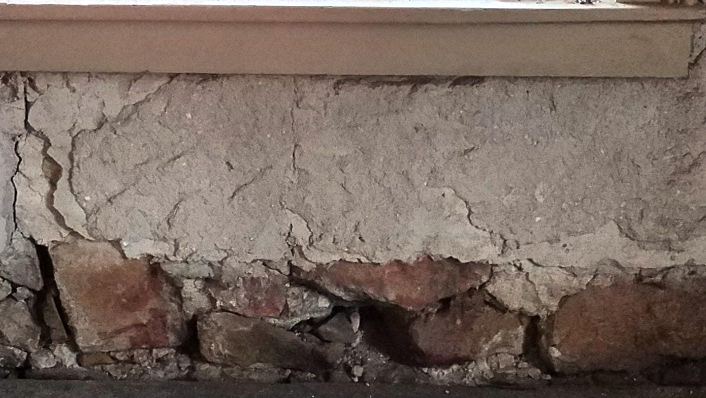 missing plaster near the floor shows reddish-colored rocks