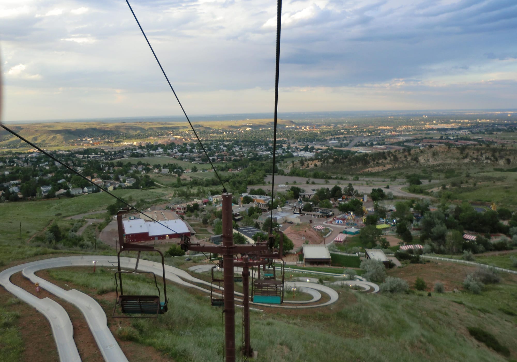 looking down a mountain with a ski lift above and a pair of concrete alpine slide tracks below