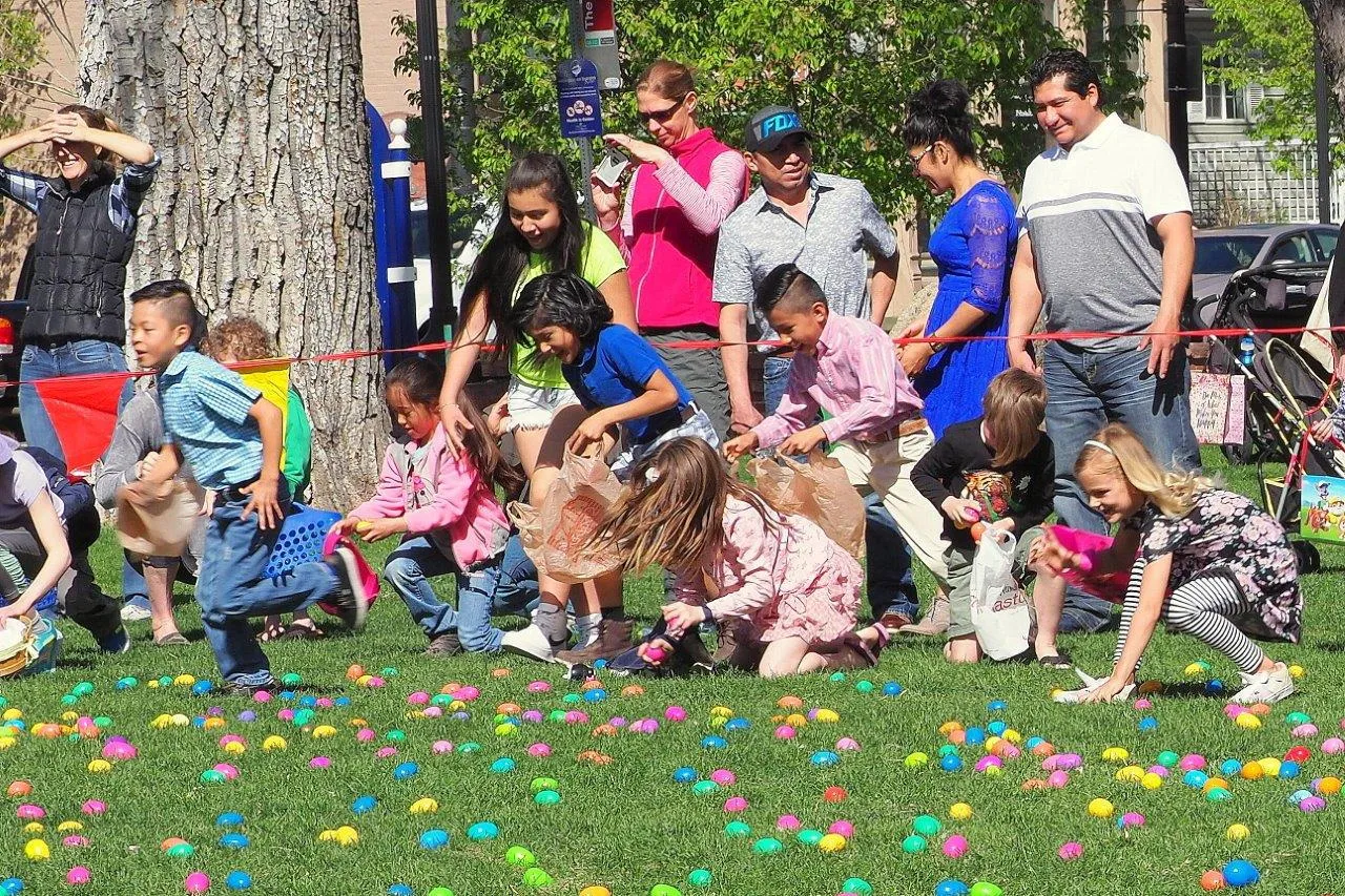 Children picking up colored plastic Easter eggs. Adults standing behind a plastic rope.