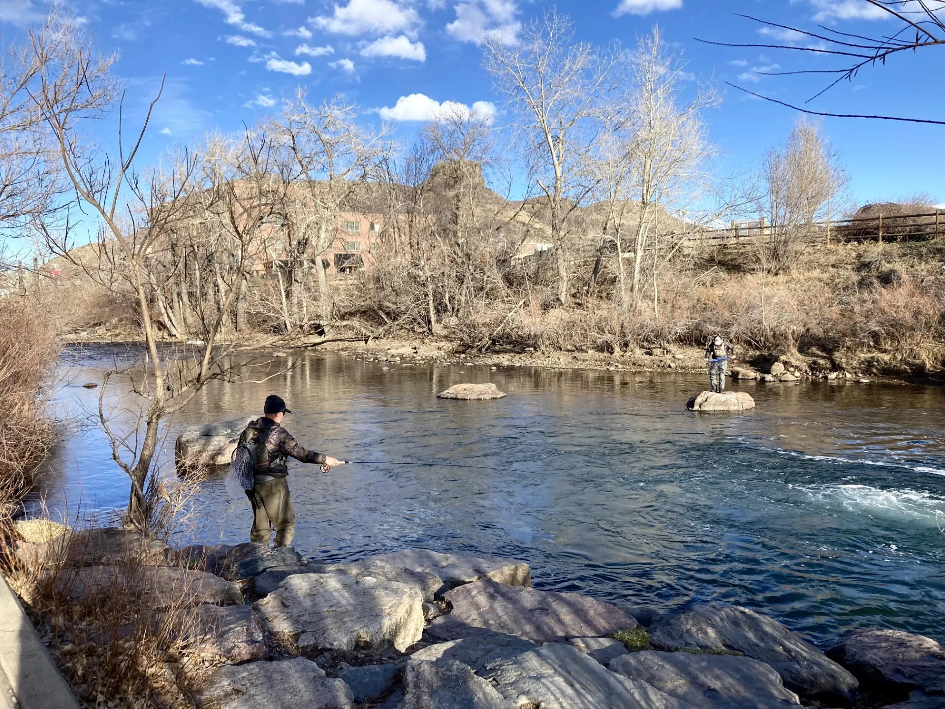 Two fishermen, dressed for cold whether, sand on rocks, fishing in Clear Creek.