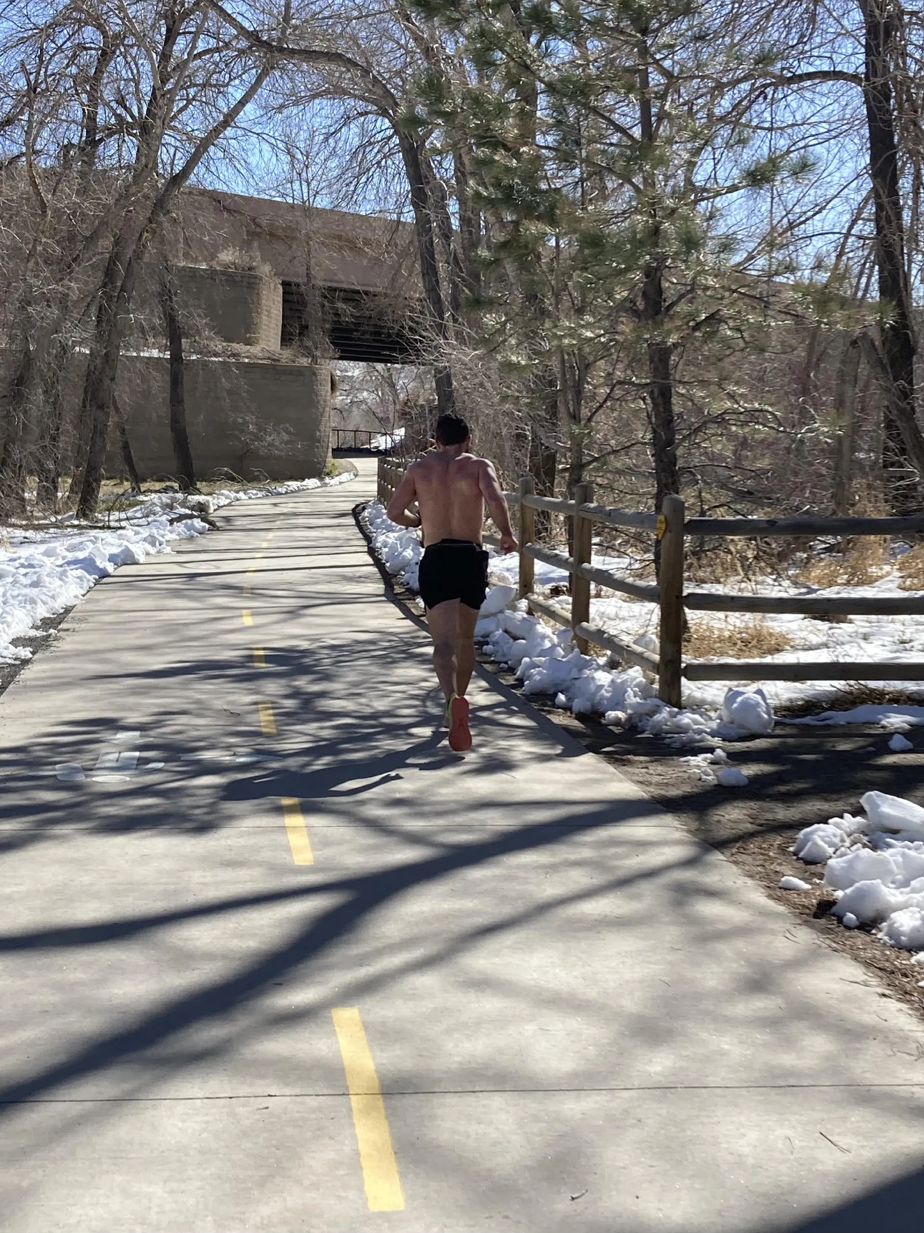 A shirtless male runner on the Clear Creek Trail - bright sun with snow at the sides of the trail