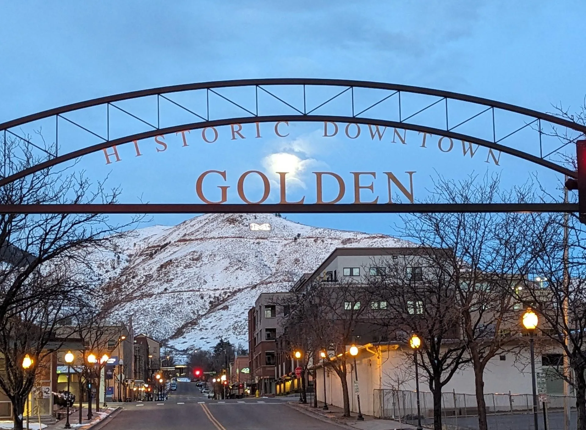 iron archway over 13th street says "Historic Downtown Golden."  Snow-covered Mt. Zion and a setting moon in background.