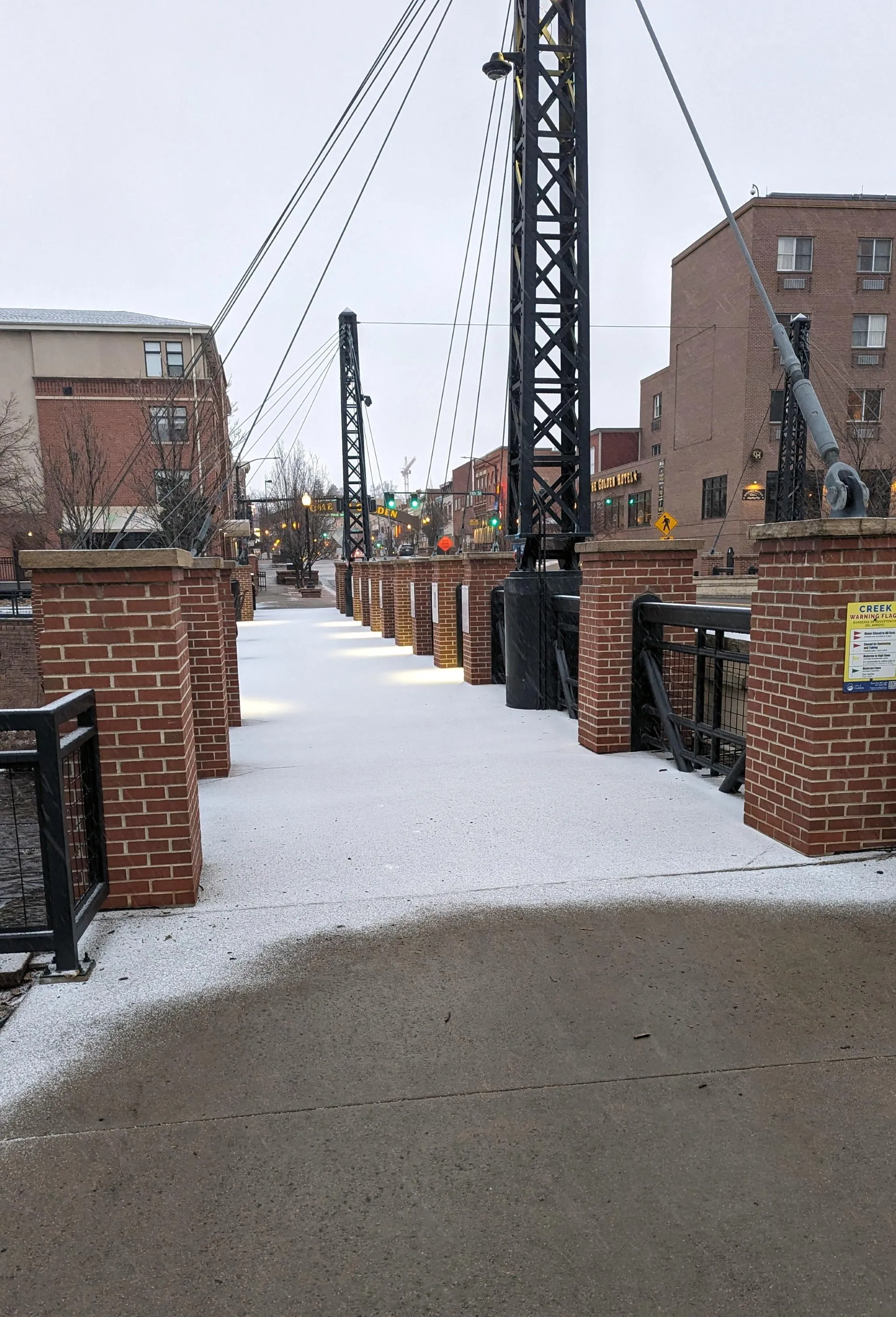 Sidewalk over the bridge is covered with snow, while the sidewalk on land is thawed.