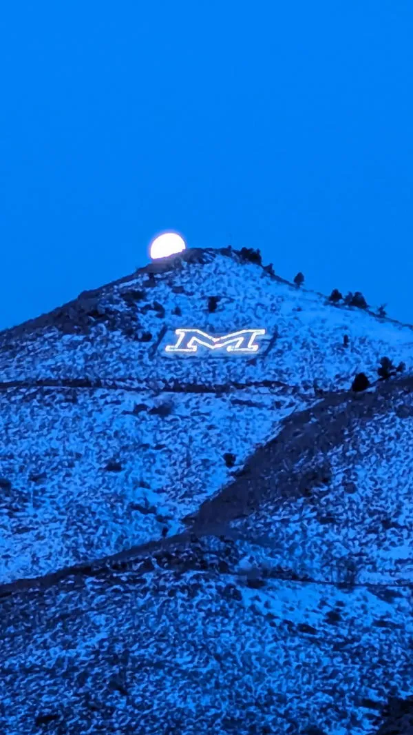 very early morning shot of Mount Zion with the M illuminated, snow onthe mountain and moon setting above