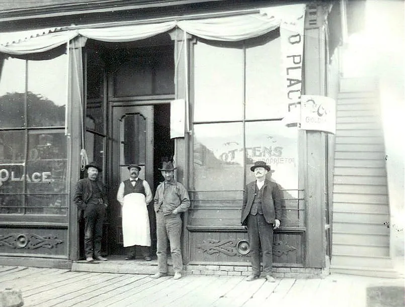 4 men stand in front of a saloon.  "Ottens Place" is painted on the windows.