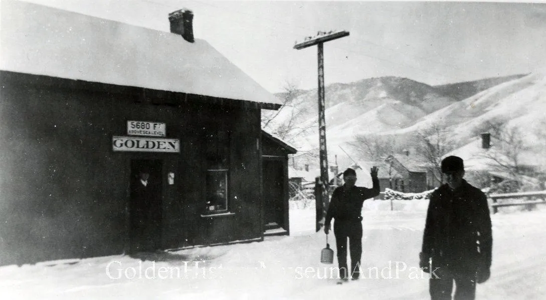 Two men stand in snow in from of the Golden express freight depot. Sign on depot says 5680 Ft above sea level.