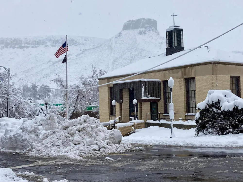 Golden post office - snow on roof and in street - American flag on pole, snow in air, Castle Rock in background