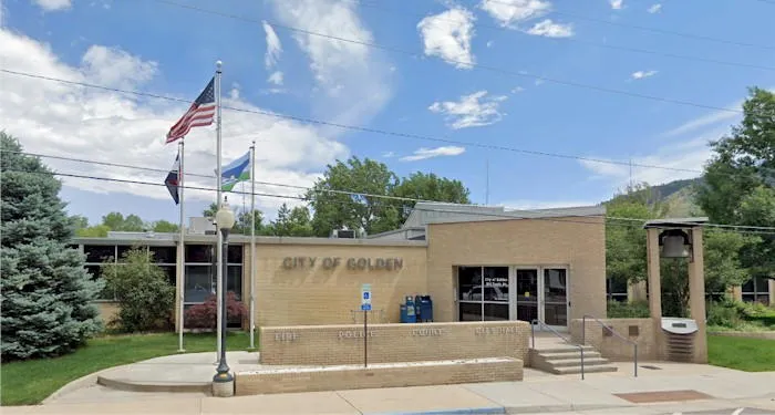 single story building of blonde brick saying CITY OF GOLDEN with three flags on poles left of door 