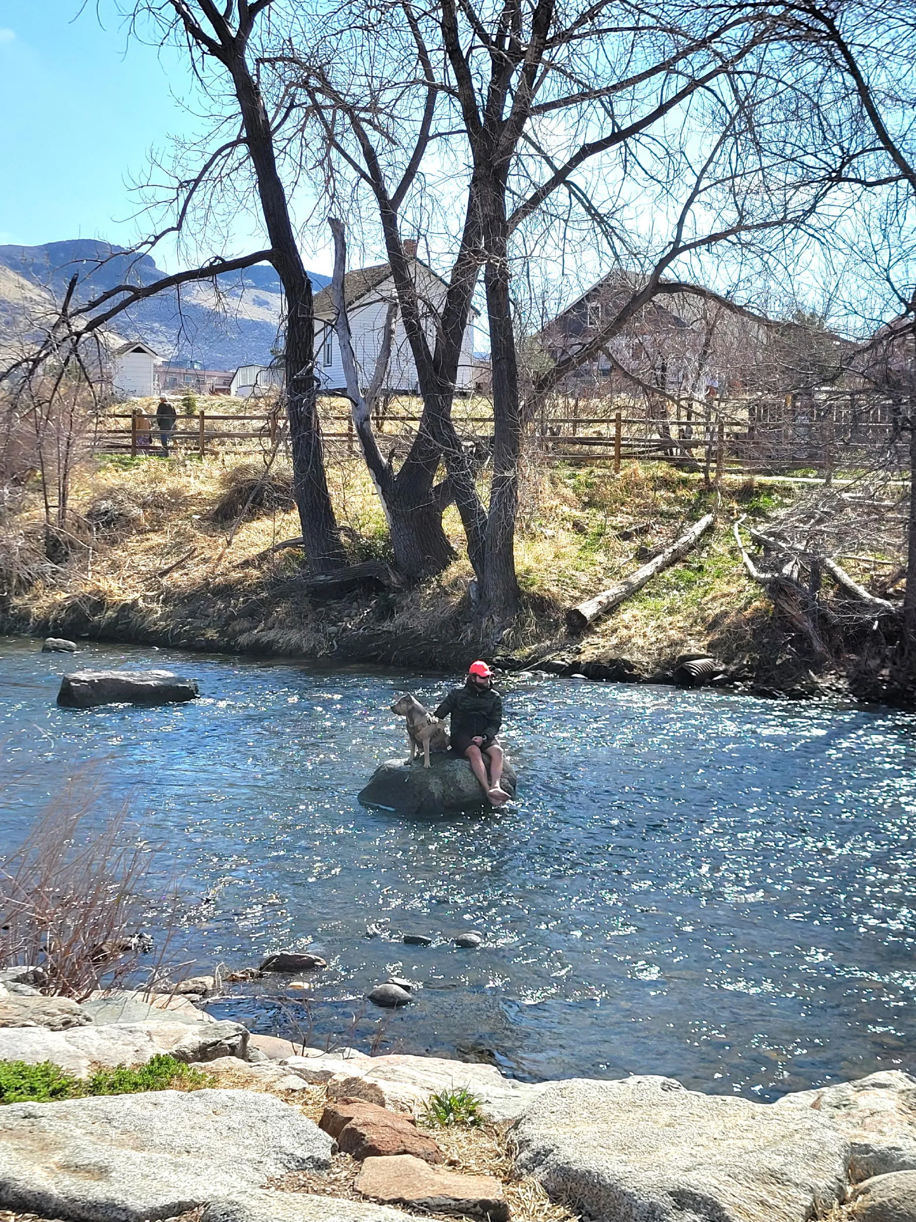 Man and dog set on a boulder in the middle of Clear Creek.  Guy Hill Schoolhouse in background.