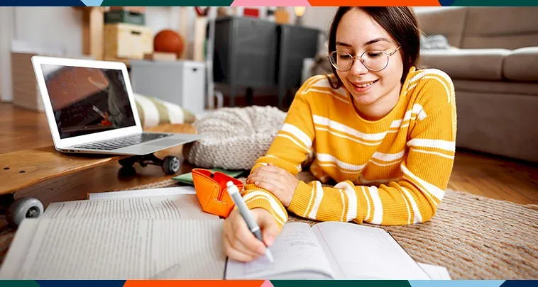Young girl writng in a journal with a laptop computer nearby. 