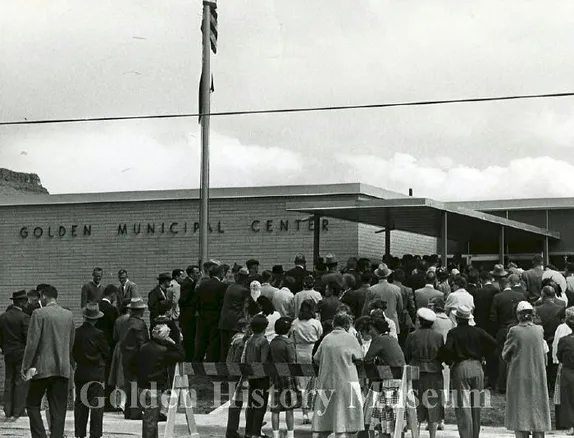 Black and white photo showing crowd of people with backs to camera, facing Golden Municipal Center