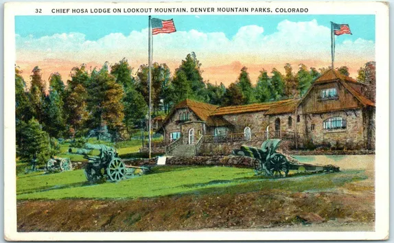 Old hand-tinted postcard showing Chief Hosa Lodge (stone construction) with 2 cannons in front and American flags