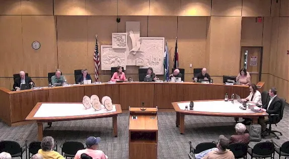 8 people behind a dais, 2 more at a table in front and to the right.  Several audience members.