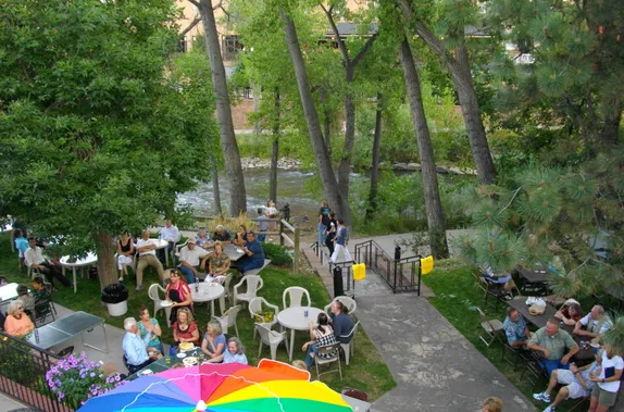 party behind the Visitors Center.  People sitting at white plastic tables under the trees.  Clear Creek in the background.
