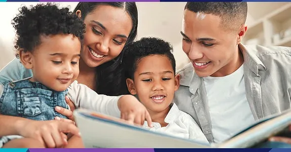 2 small children and 2 young adults looking at a book and smiling