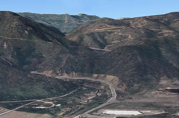 Two-lane paved road heading into the mountains.  Higher up, older, unpaved switchback roads are visible.