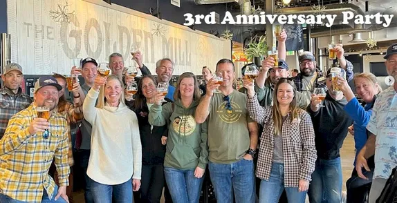 large group holding beers in a toast, standing in front of The Golden Mill sign