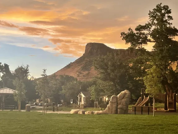 view across a small park with a small play structure and small pavilion.  Castle Rock and setset clouds in the background