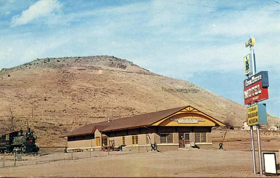 Tall sign advertising the Motel and Museum.  Depot, steam engine, and North Table Mountain in the background.