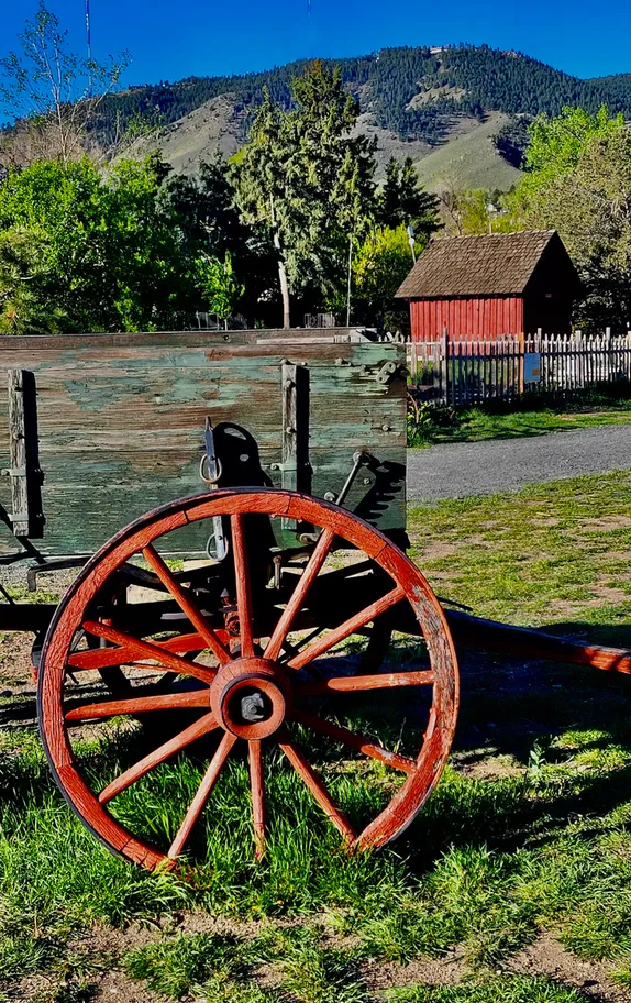 wagon with a red-painted wheel and tongue in the foreground; red barn and mountains in the background