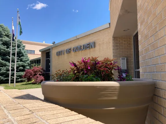 blond brick building saying "CITY OF GOLDEN" with large pot of coleus in the foreground